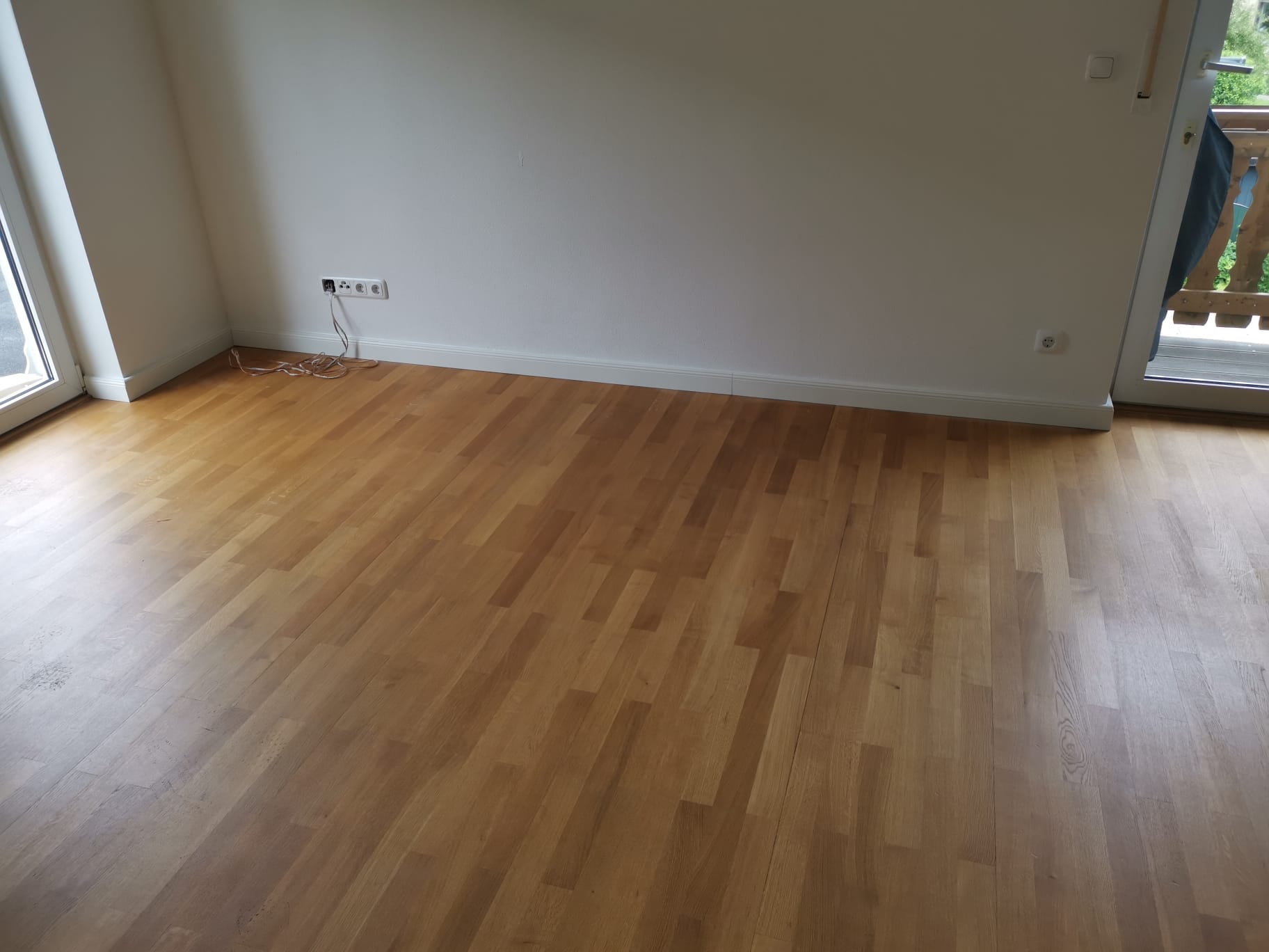 Frisch verlegter, hochwertiger Parkettboden in einem Zimmer mit Zugang zu einem Balkon, der natürliches Licht hereinlässt.